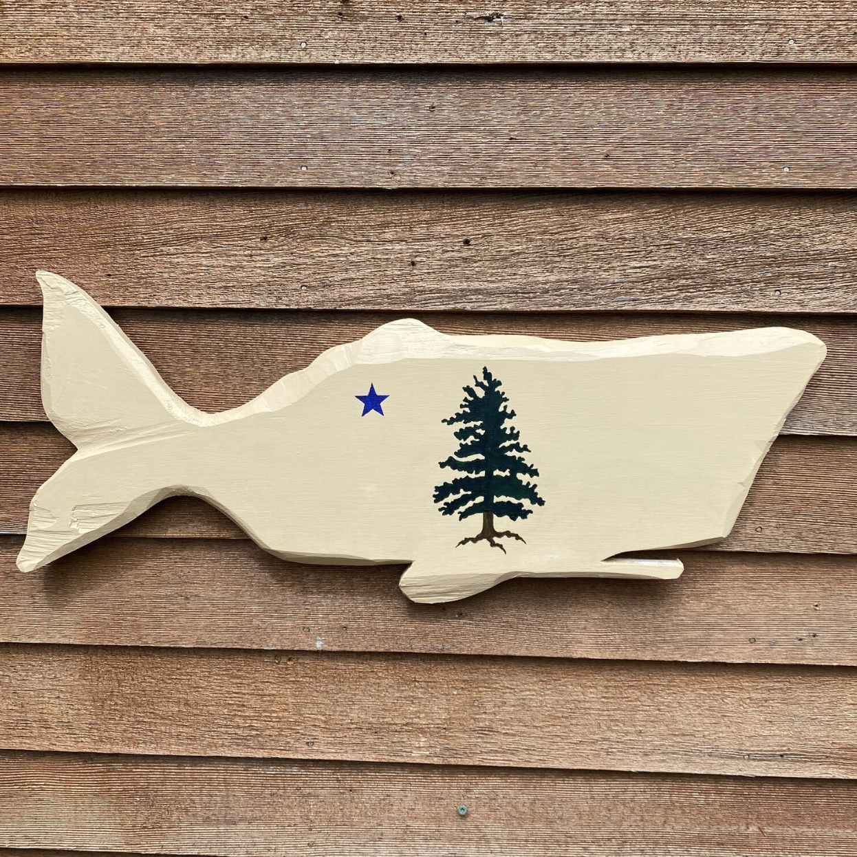 Wood carving of a whale, painted with the 1901 Maine Flag on a wood clapboard wall