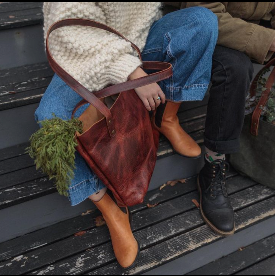 Rogue Industries deep red leather tote back in a women's lap sitting on rustic black wooden steps